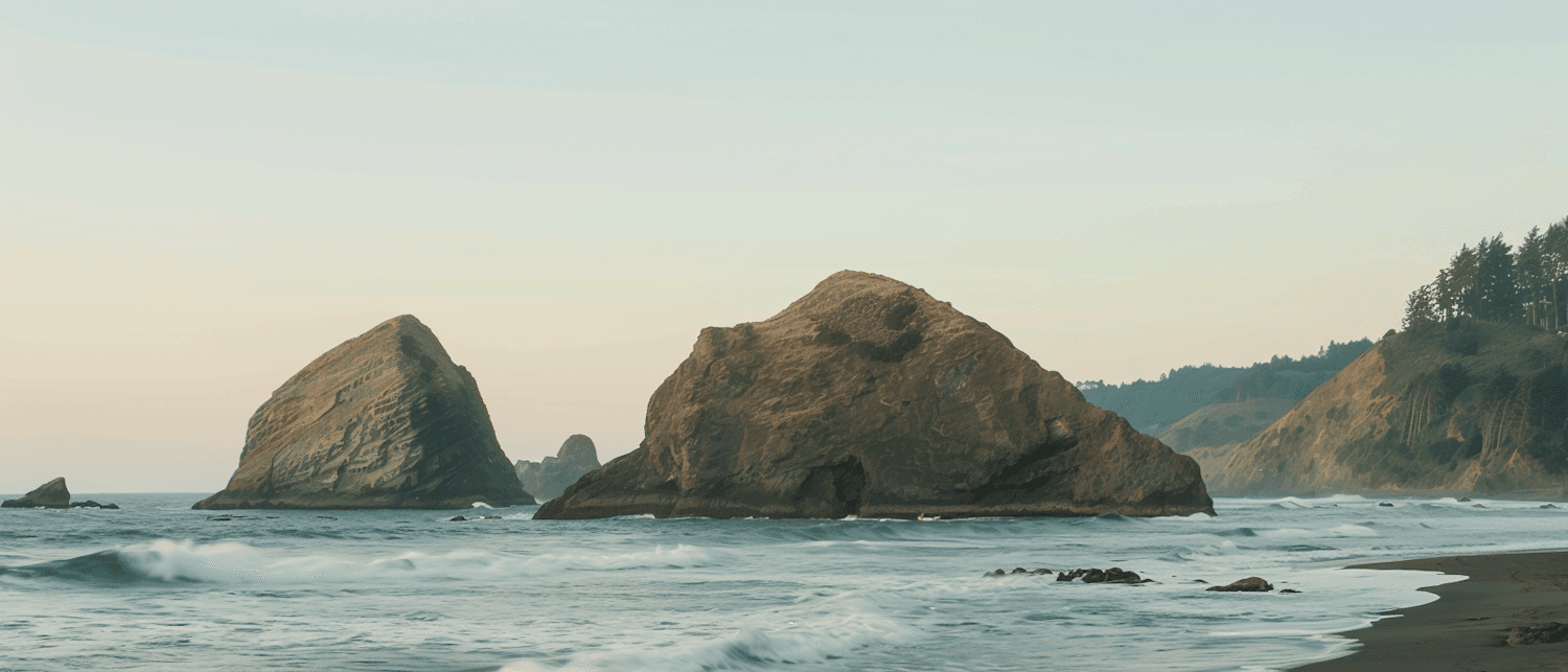 Rugged coastal rocks meeting gentle surf beneath a pastel sky